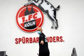 Physiotherapeut Christian Osebold vom 1. FC Köln steht mit Mundschutz vor einem Klub-Logo: In der Corona-Krise unterstützt der Bundesligist das Erzbistum Köln.