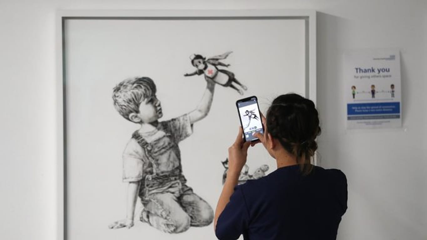 Eine medizinische Mitarbeiterin fotografiert das Banksy-Kunstwerk mit dem Titel "Game Changer".