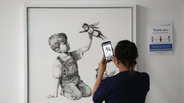 Eine medizinische Mitarbeiterin fotografiert das Banksy-Kunstwerk mit dem Titel "Game Changer". Eine medizinische Mitarbeiterin fotografiert das Banksy-Kunstwerk mit dem Titel "Game Changer".