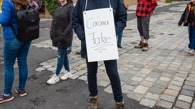 Eine Teilnehmerin trägt bei einer Demo gegen die Corona-Maßnahmen ein Schild mit der Aufschrift "Corona Fake". Eine Teilnehmerin trägt bei einer Demo gegen die Corona-Maßnahmen ein Schild mit der Aufschrift "Corona Fake".