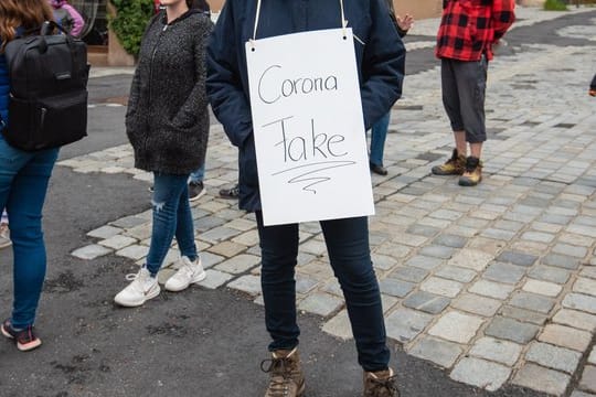 Eine Teilnehmerin trägt bei einer Demo gegen die Corona-Maßnahmen ein Schild mit der Aufschrift "Corona Fake".