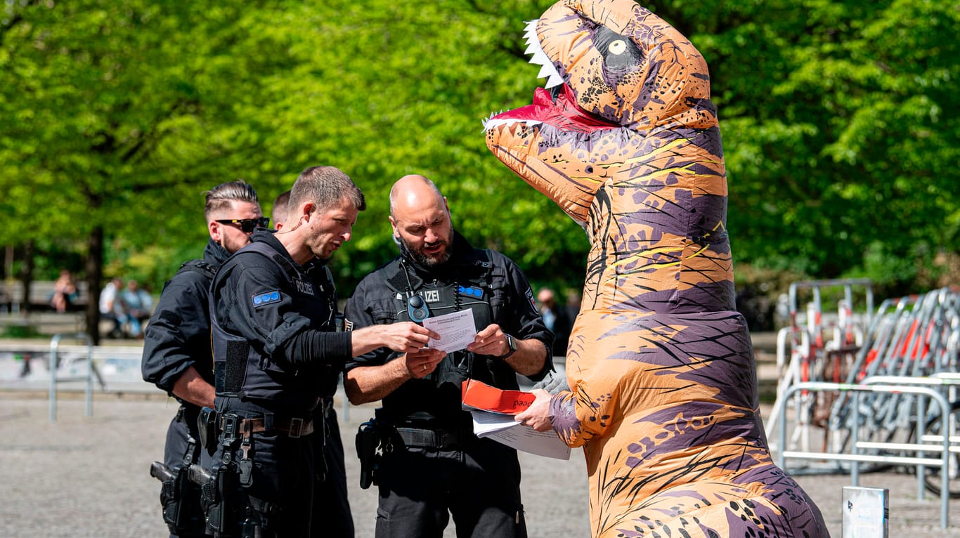 Berlin: Polizisten sprechen auf der Demonstration gegen die Hygienedemo auf dem Rosa-Luxemburg-Platz mit einem Aktivisten in einem Dinosaurierkostüm.