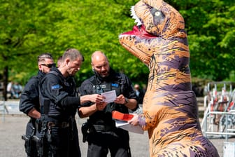 Berlin: Polizisten sprechen auf der Demonstration gegen die Hygienedemo auf dem Rosa-Luxemburg-Platz mit einem Aktivisten in einem Dinosaurierkostüm.