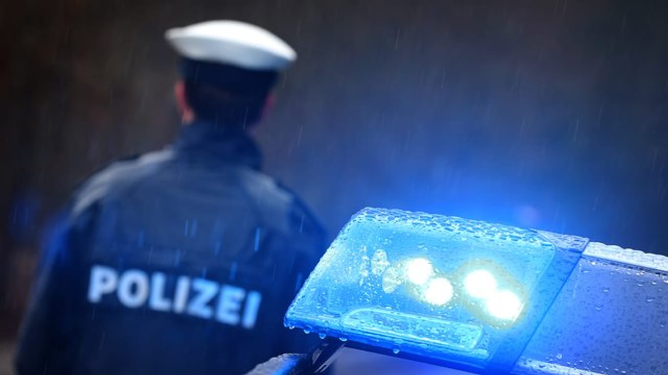 Ein Polizist vor einem Streifenwagen mit aktiviertem Blaulicht.