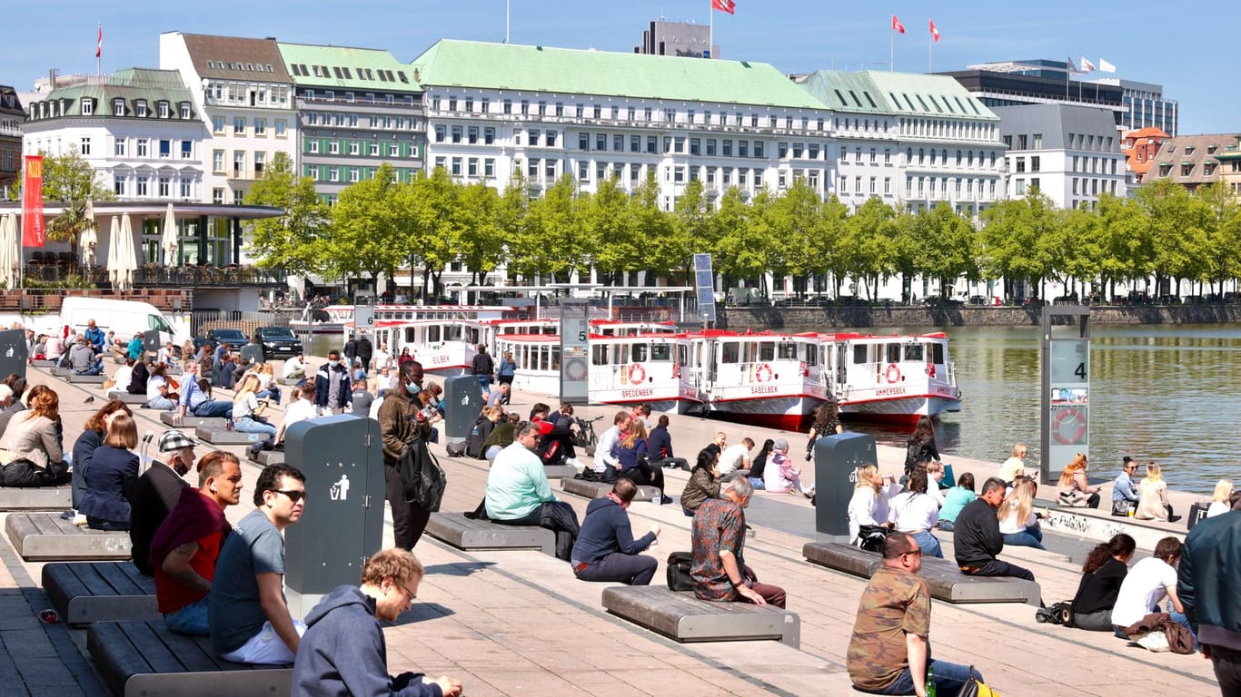 Passanten sitzen an der Binnenalster: Das sonnige Wetter lockt die Menschen nach draußen.