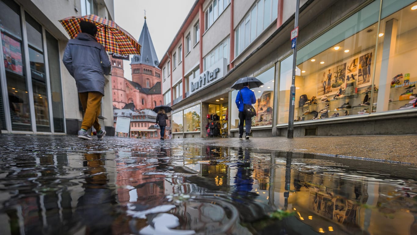 Menschen gehen bei Regen durch eine Mainzer Einkaufsstraße in Richtung Dom: Viele kaufen nur das Nötigste und verzichten auf gemütliches Bummeln.
