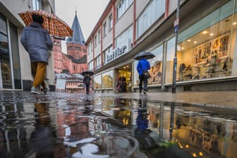 Menschen gehen bei Regen durch eine Mainzer Einkaufsstraße in Richtung Dom: Viele kaufen nur das Nötigste und verzichten auf gemütliches Bummeln.