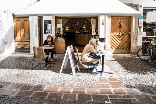 Frauen mit Mundschutz trinken Kaffee vor einer Bar in Bozen.
