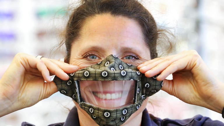 Die Geschäftsführerin eines Hörgeräte-Geschäfts Sandra Bagus hält eine Maske mit Sichtschutz: Ihre Kunden können sie durch das Sehen der Lippenbewegungen besser verstehen.