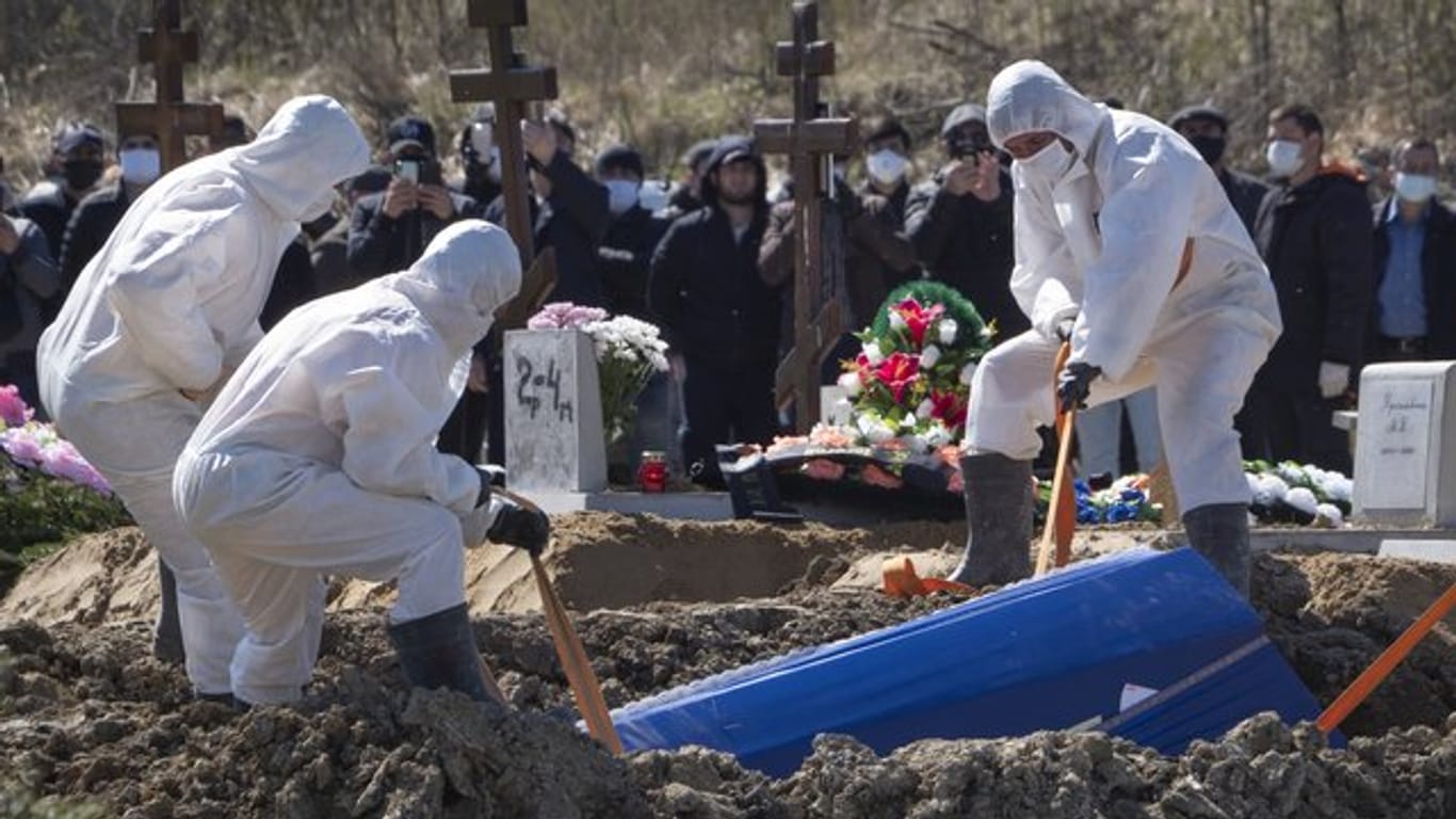 Totengräber in Schutzkleidung lassen auf einem Friedhof im russischen Kolpino den Sarg eines Covid-19-Opfers in ein Grab hinab.