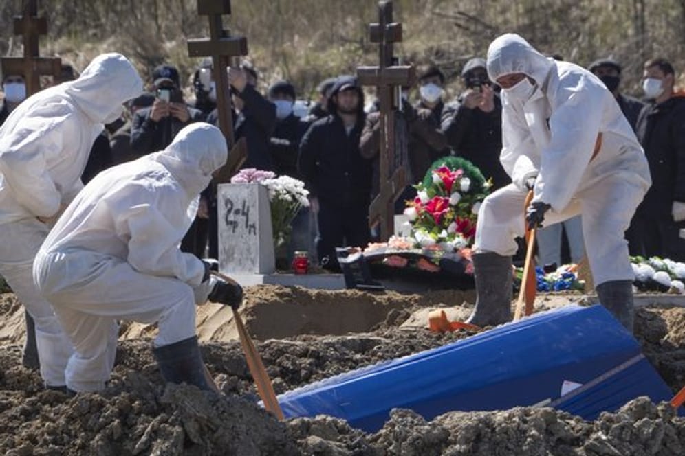 Totengräber in Schutzkleidung lassen auf einem Friedhof im russischen Kolpino den Sarg eines Covid-19-Opfers in ein Grab hinab.