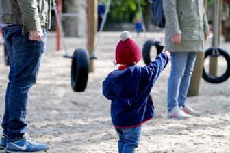 Ein Kind spielt mit seinen Eltern auf einem Spielplatz.