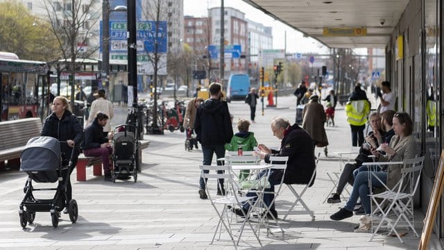 Menschen sitzen im Stadtzentrum von Stockholm vor einem Eiscafe.