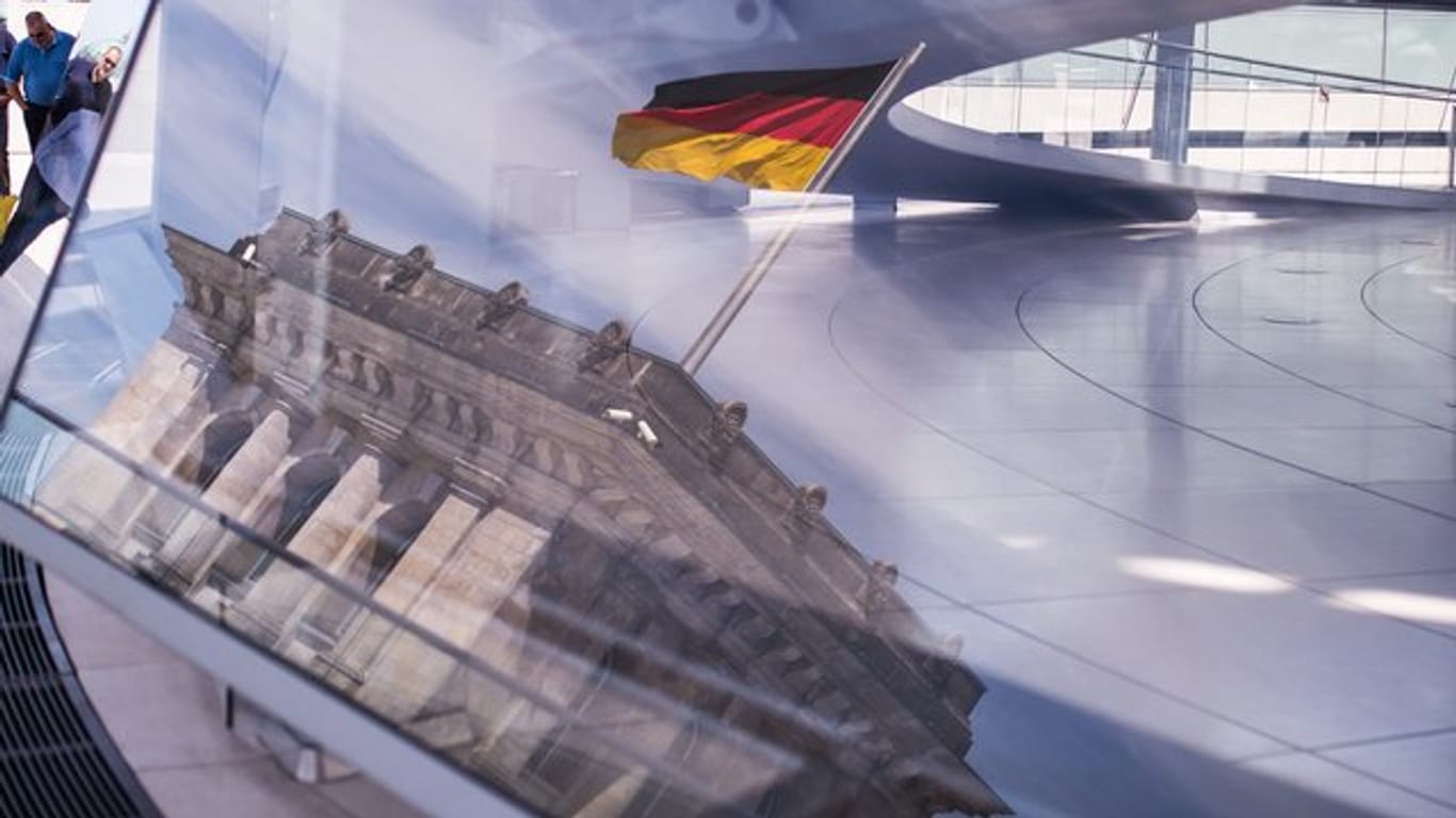 Eine Deutschland-Fahne spiegelt sich in der Kuppel des Reichstagsgebäudes.