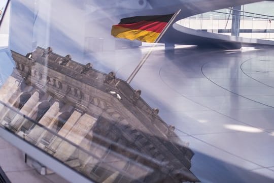 Eine Deutschland-Fahne spiegelt sich in der Kuppel des Reichstagsgebäudes.