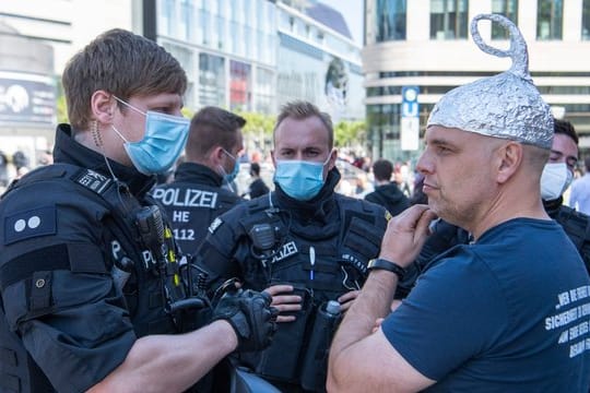 Polizisten erteilen einem Mann mit einem Alu-Hut einen Verweis
