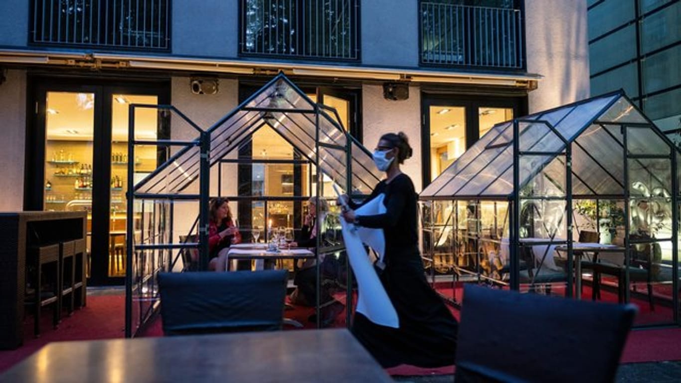 Gäste sitzen an Tischen in kleinen Gewächshäusern, während die Kellnerin einen Tisch abdeckt: Mit kreativen Lösungen reagieren Düsseldorfer Gastronomen auf die strengen Hygienevorschriften in der Corona-Krise.