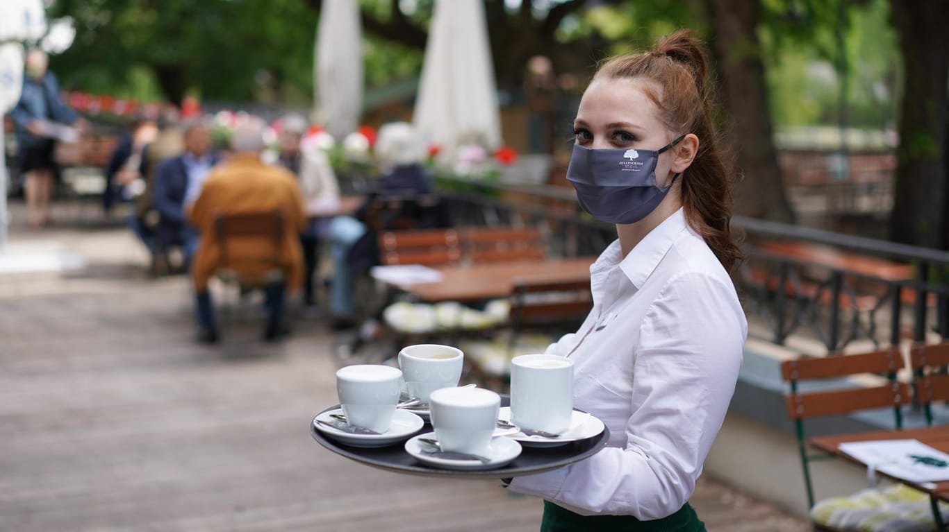 Eine Kellnerin mit Gesichtsmaske serviert in Berlin Kaffee.