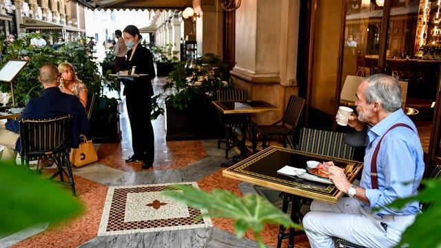Gäste sitzen mit Abstand zueinander an Tischen in einem Café in Mailand. Gäste sitzen mit Abstand zueinander an Tischen in einem Café in Mailand.