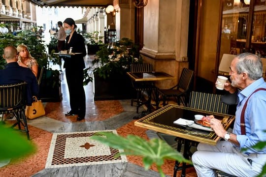 Gäste sitzen mit Abstand zueinander an Tischen in einem Café in Mailand.