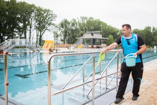 Freibad: Der Schwimmmeister Björn Bendias in Ochtrup desinfiziert zwischen zwei Schwimmzeiten die Handläufe neben dem Schwimmbecken.