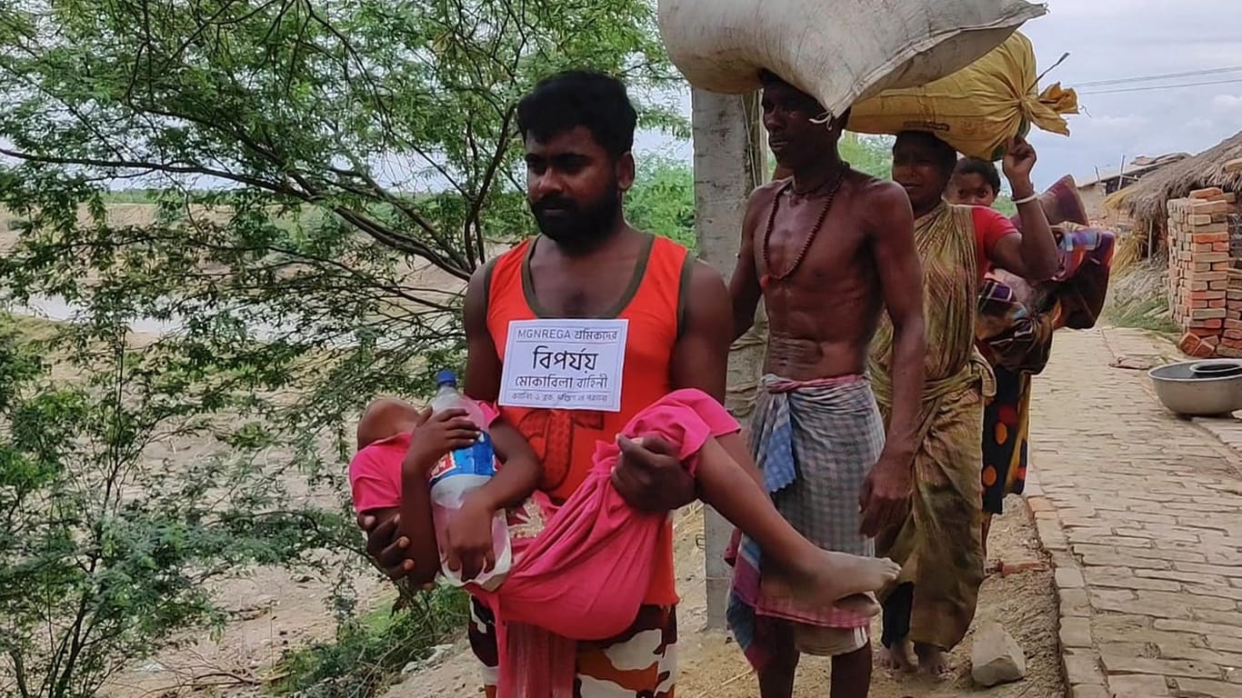 Ein Freiwilliger des Katastrophenschutzes trägt bei der Evakuierung von Bewohnern eines Dorfes in Indien ein krankes Kind auf dem Arm.