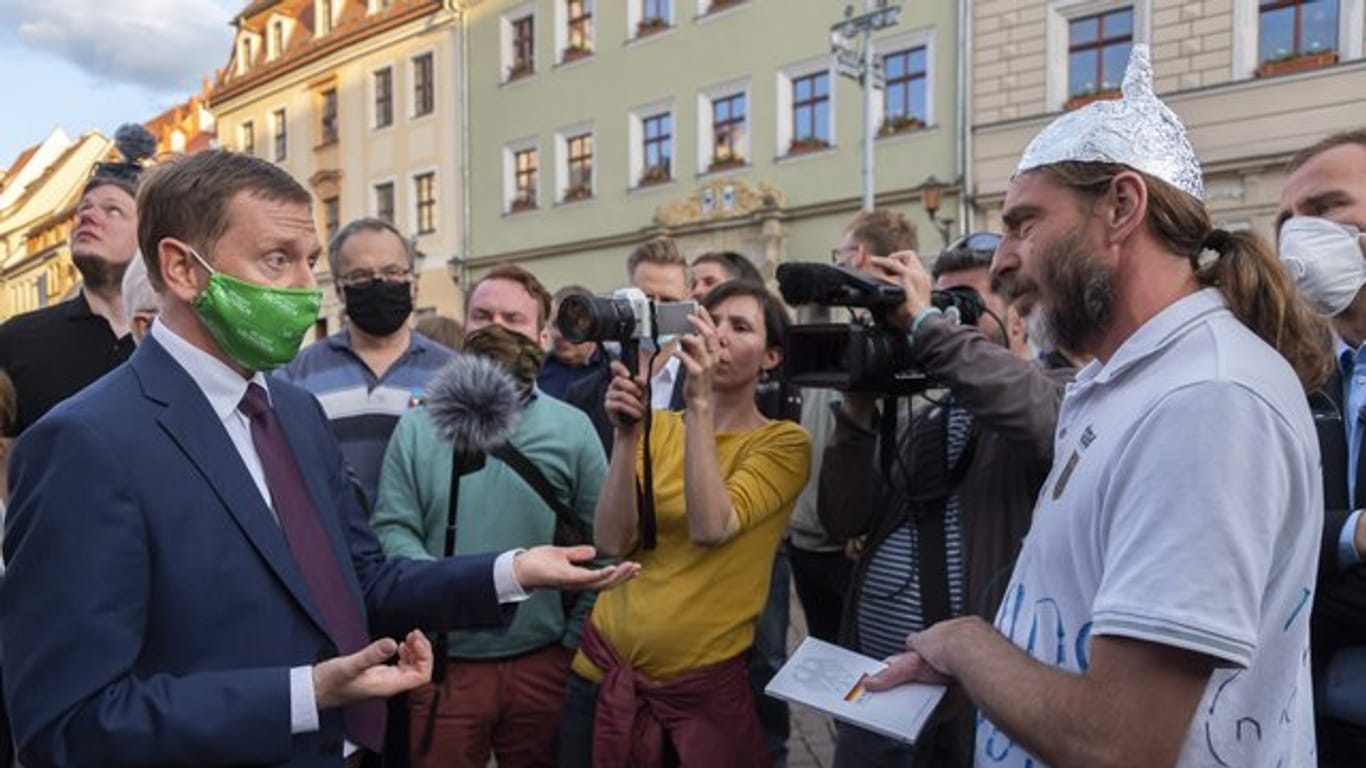 Sachsens Ministerpräsident Michael Kretschmer (l) spricht in Pirna mit einem Gegner der Corona-Maßnahmen.