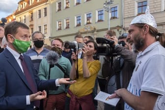 Sachsens Ministerpräsident Michael Kretschmer (l) spricht in Pirna mit einem Gegner der Corona-Maßnahmen.