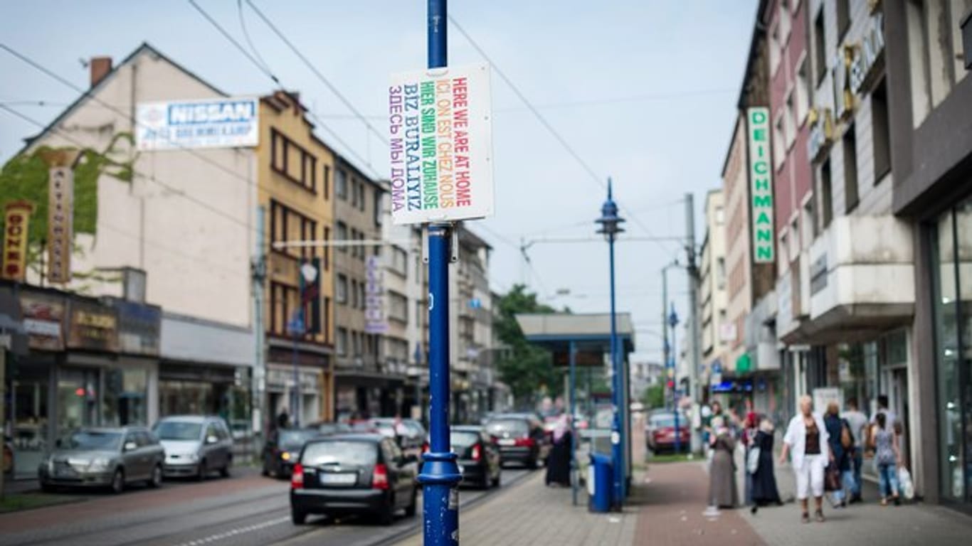 Ein Schild "Hier sind wir zuhause" in verschiedenen Sprachen hängt in Duisburg auf der Straße.