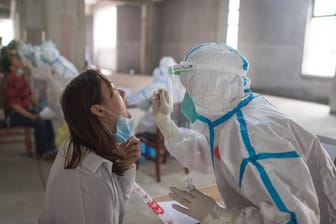 Eine Frau wird in Wuhan von einer Person in Schutzanzug auf das Coronavirus getestet.