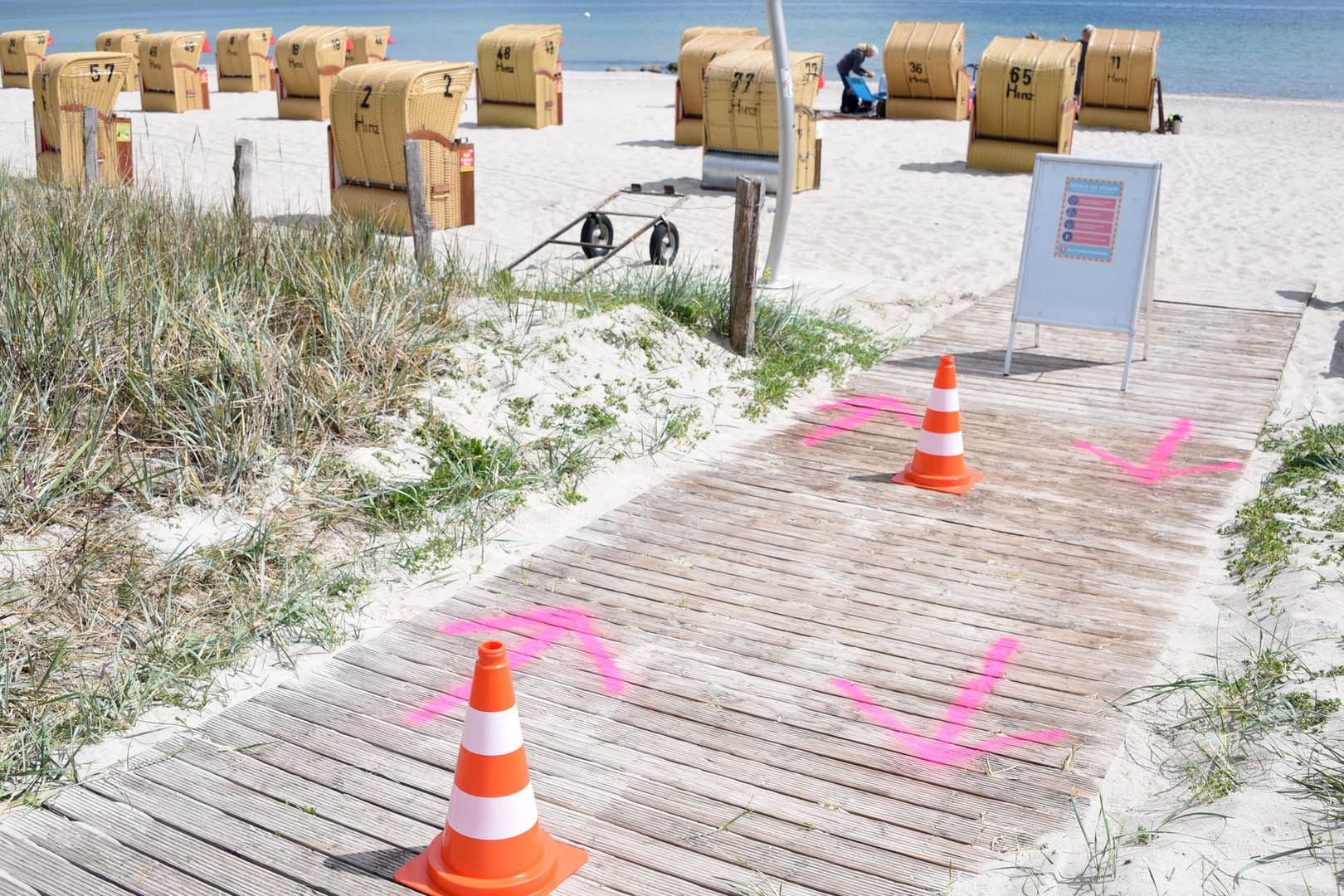 Haffkrug (Schleswig-Holstein,: Auf den Boden gesprühte Pfeile und Pylonen regeln den Zugang zum Strand an der Ostsee.