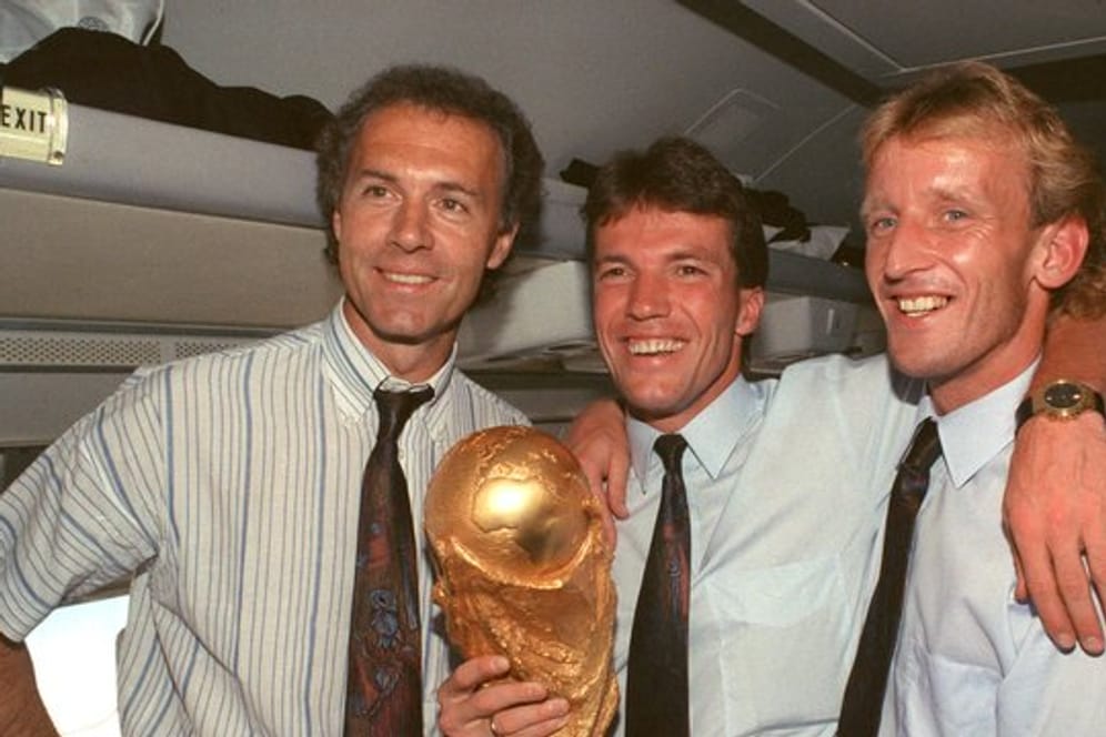 Auf dem Rückflug von Rom präsentieren DFB-Teamchef Franz Beckenbauer (l), Kapitän Lothar Matthäus (M) und Andreas Brehme den WM-Pokal.