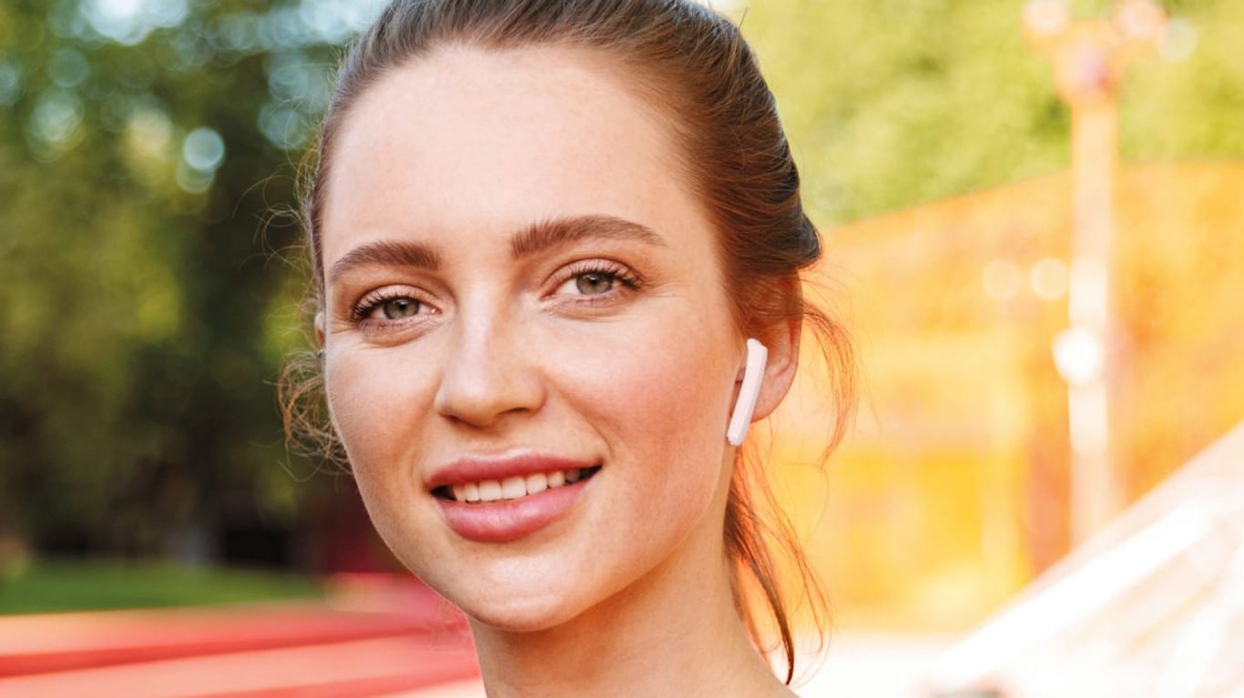 Junge Frau mit einem weißen Ohrhörer im Ohr: Aldi bietet günstige True-Wireless-Kopfhörer.