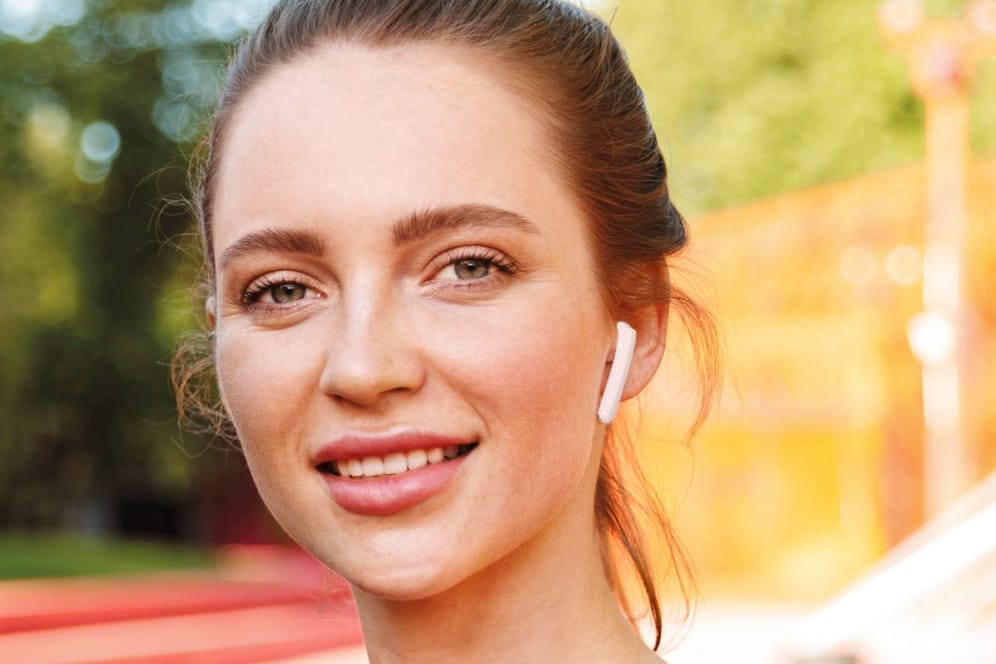 Junge Frau mit einem weißen Ohrhörer im Ohr: Aldi bietet günstige True-Wireless-Kopfhörer.
