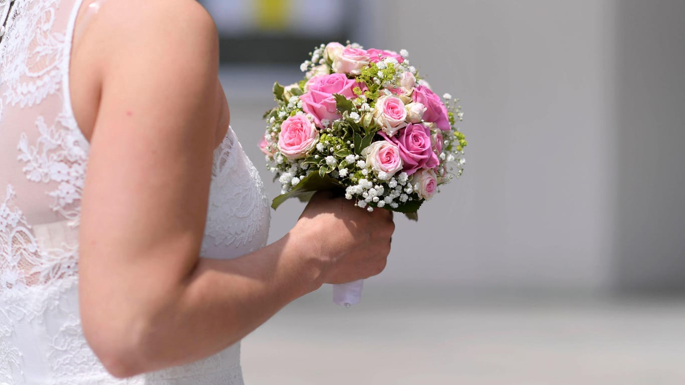 Eine Frau in einem weißen Kleid mit Blumenstrauß: Eine Braut ist wegen eines Hochzeitskleides in Nürnberg vor Gericht gezogen.
