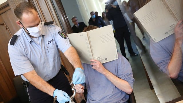 Ein Justizbeamter nimmt dem Angeklagten vor Prozessbeginn die Handschellen ab. Ein Justizbeamter nimmt dem Angeklagten vor Prozessbeginn die Handschellen ab.