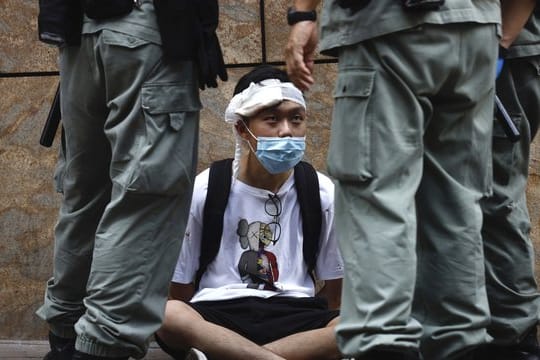 Bereitschaftspolizisten stehen im Hongkonger Central District um einen auf dem Boden sitzenden Demonstranten.