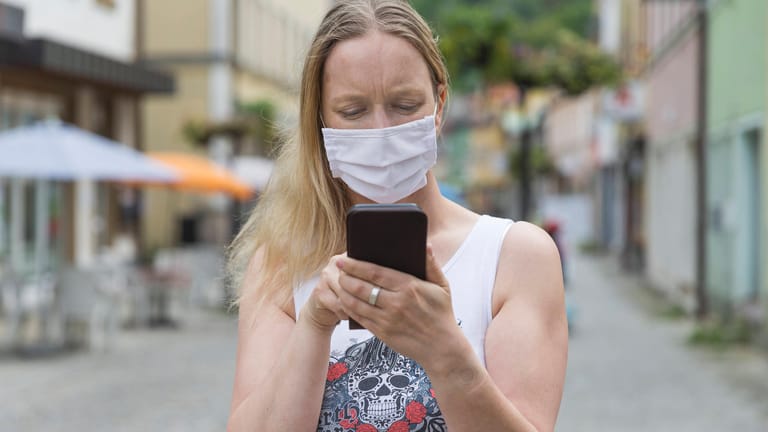 Eine Frau mit Mund-Nase-Schutz bedient ein Smartphone: Android-Handys haben jetzt eine Schnittstelle für Corona-Warn-Apps.
