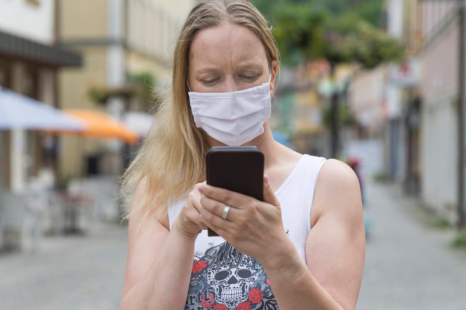 Eine Frau mit Mund-Nase-Schutz bedient ein Smartphone: Android-Handys haben jetzt eine Schnittstelle für Corona-Warn-Apps.
