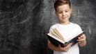 Ein Junge steht mit einem Buch vor einer Tafel