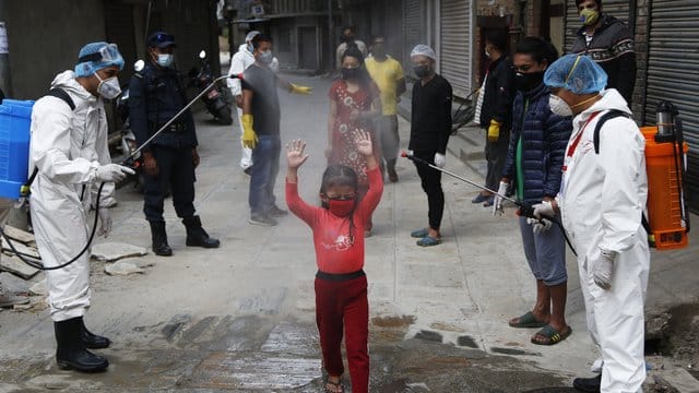 Ein Mädchen in Nepal wird mit Desinfektionsmittel besprüht.