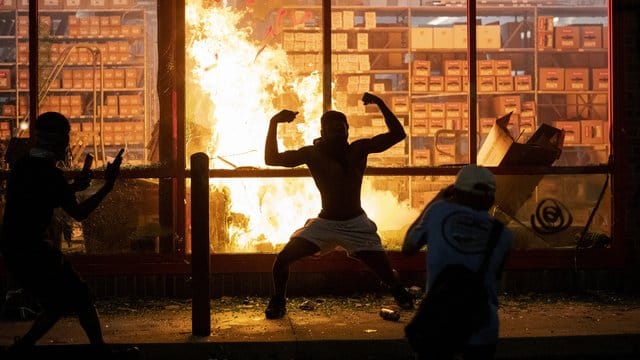 Ein Mann posiert während der gewaltsamen Proteste in Minneapolis vor einem Feuer einem Geschäft. Ein Mann posiert während der gewaltsamen Proteste in Minneapolis vor einem Feuer einem Geschäft.