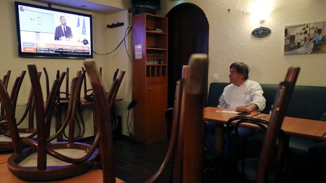 Ein Restaurantbesitzer schaut sich in Paris auf einem Nachrichtensender eine Fernsehansprache des französischen Premierministers Philippe an. Ein Restaurantbesitzer schaut sich in Paris auf einem Nachrichtensender eine Fernsehansprache des französischen Premierministers Philippe an.