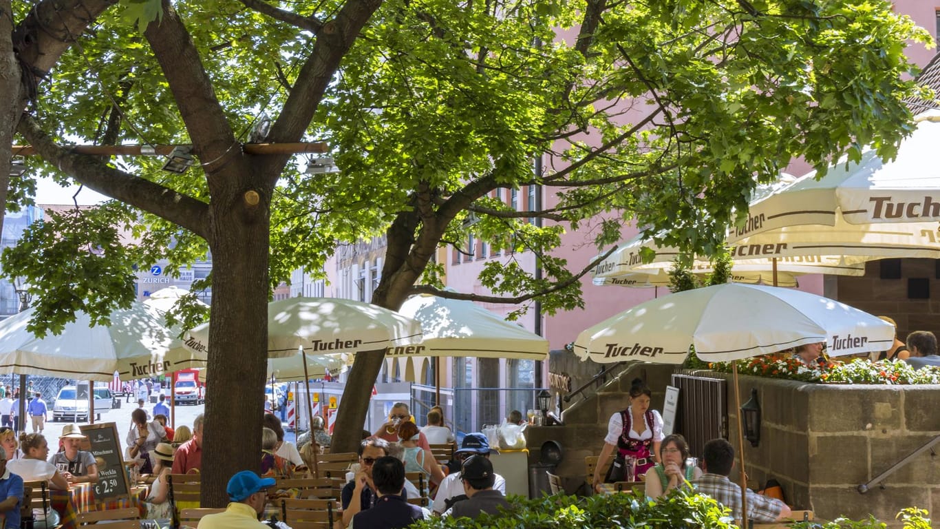 Menschen sitzen unter einem Baum im Biergarten: Unter Auflagen dürfen Biergärten wieder öffnen.