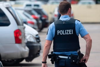 Ein Polizist geht über den Parkplatz einer Hochhaussiedlung in Dietzenbach: Nachdem am Freitag Einsatzkräfte von einer Gruppe Männer mit Steinen attackiert worden waren, gehen die Ermittlungen der Behörden nun weiter.