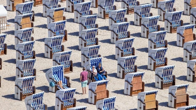 Erste Urlauber sitzen in Strandkörben am Ostseestrand in Warnemünde.