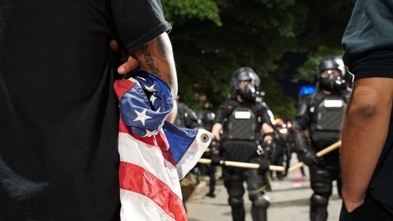 Ein Demonstrant mit einer zusammengeknüllten US-Flagge vor Polizisten: Amerika kommt nicht zur Ruhe.