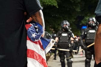 Ein Demonstrant mit einer zusammengeknüllten US-Flagge vor Polizisten: Amerika kommt nicht zur Ruhe.