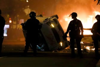 Washington: Polizisten stehen am Sonntag neben einem umgedrehten Fahrzeug, im Hintergrund lodern Flammen.