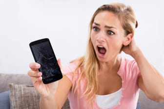 Frau starrt erschrocken auf ihr Handy: Ein Bild kann derzeit Android-Smartphones unbenutzbar machen